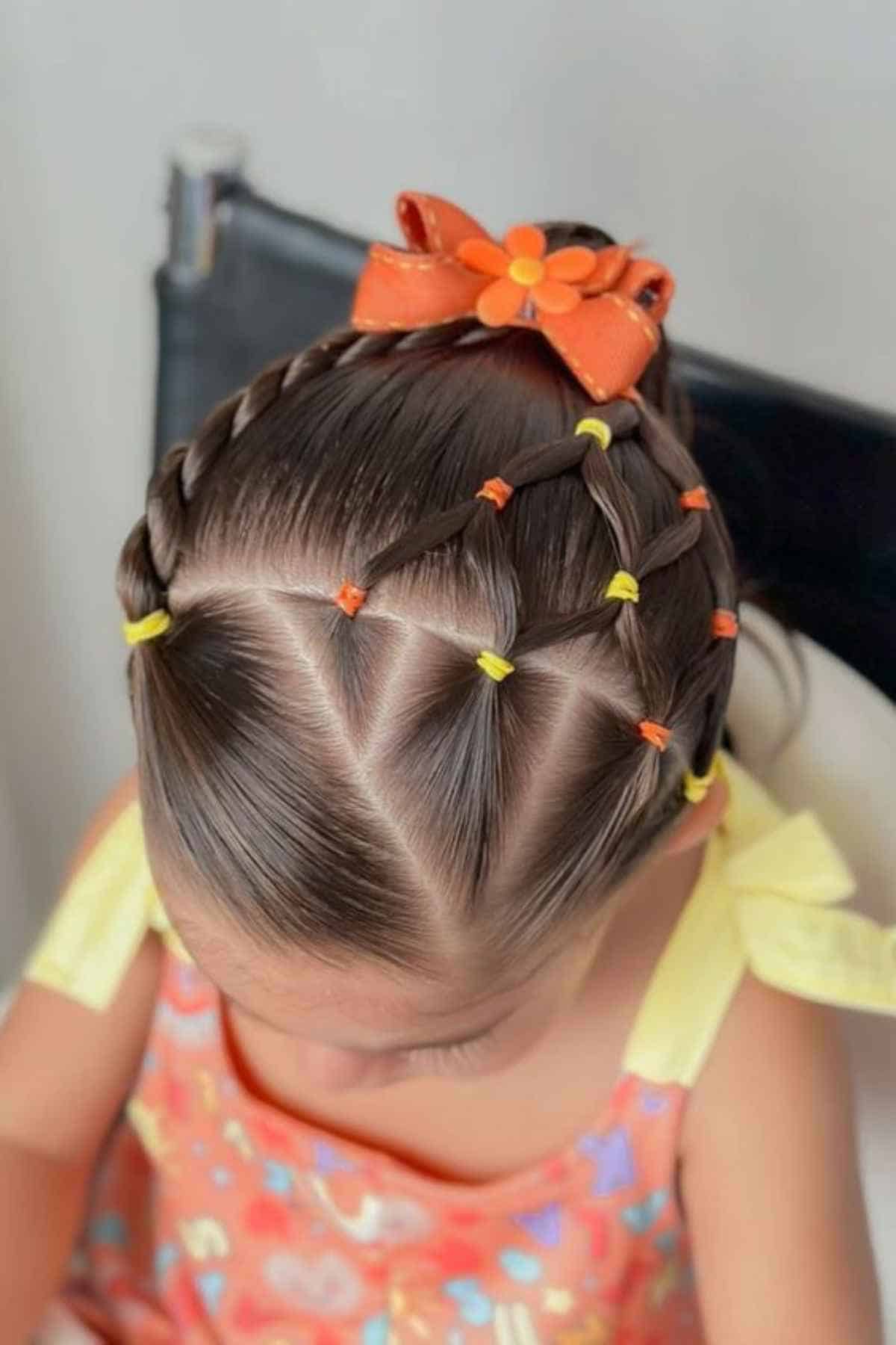A child’s hair styled in a grid pattern of small ponytails with orange and yellow elastic bands, topped with an orange bow.