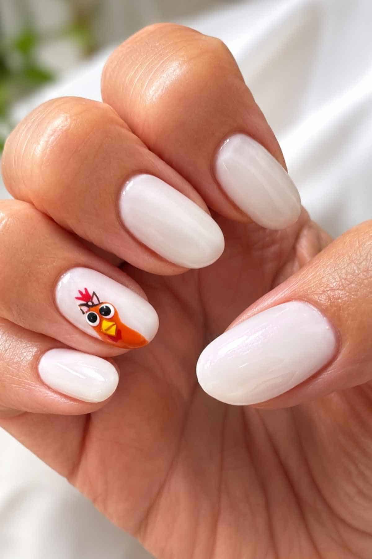 Manicured nails with glossy white polish, featuring a turkey decal on the ring finger.
