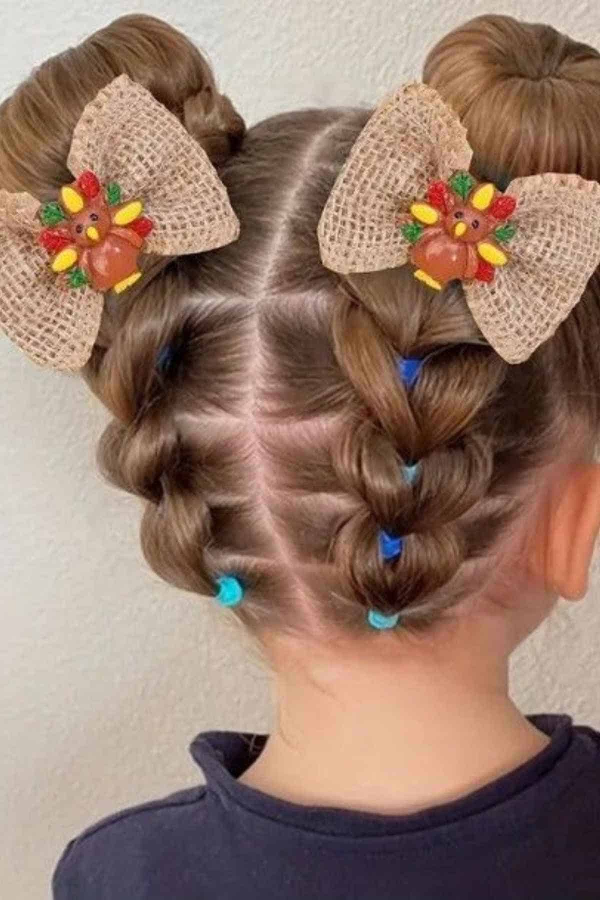 A child’s hair styled in two buns with braids, accented by burlap bows featuring turkey-shaped ornaments.
