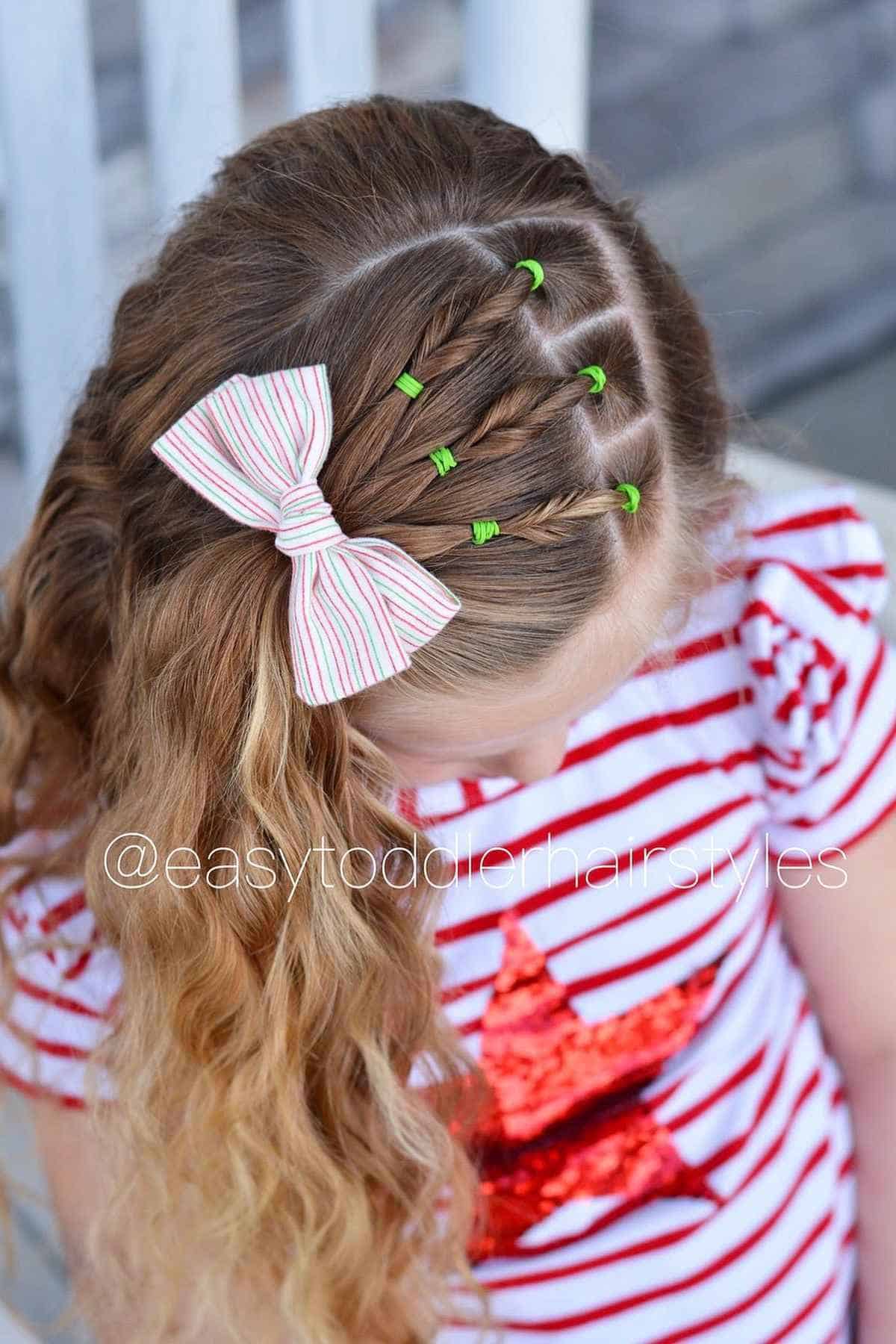 A young girl’s hair styled in small braids secured with green elastics and a striped bow.