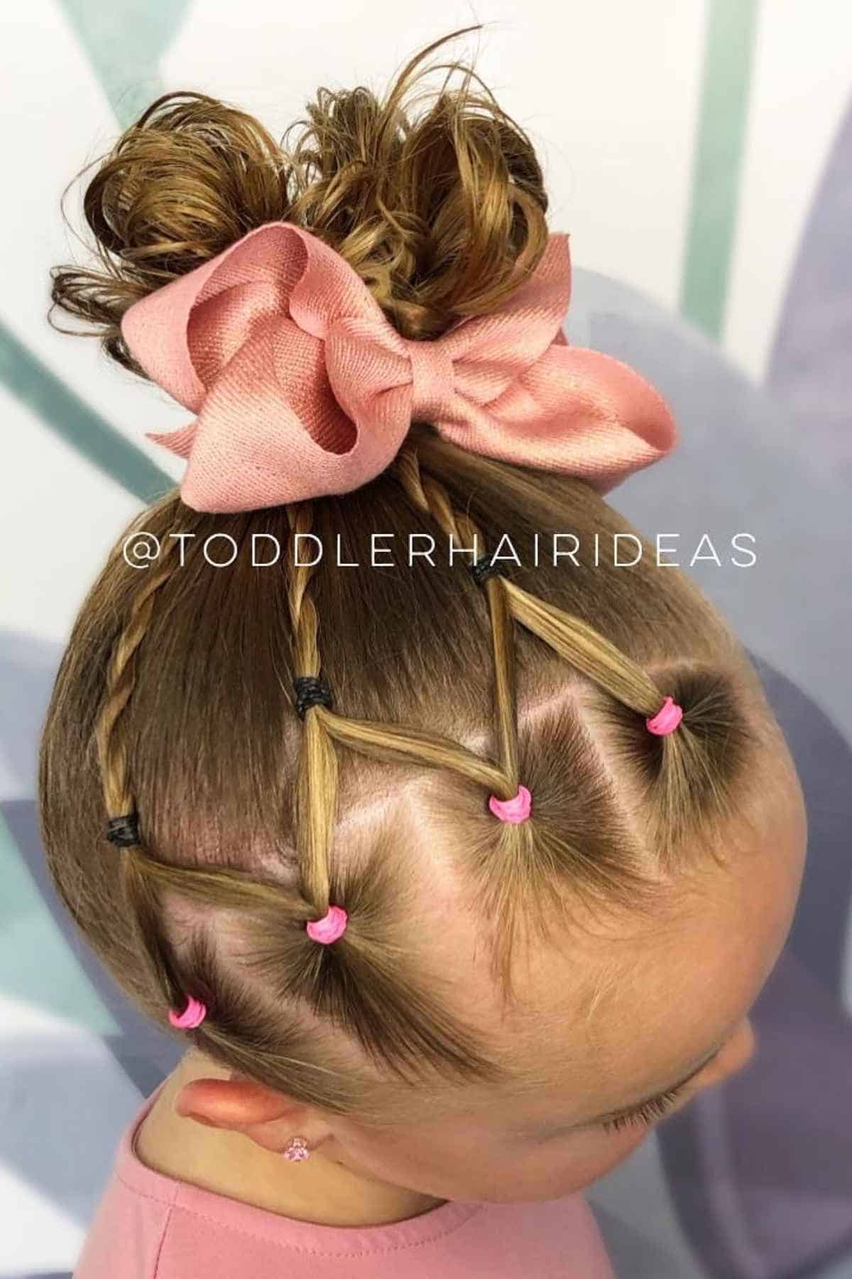 A toddler’s hairstyle featuring multiple small ponytails connected in a crisscross pattern, finished with a large pink bow at a high bun.