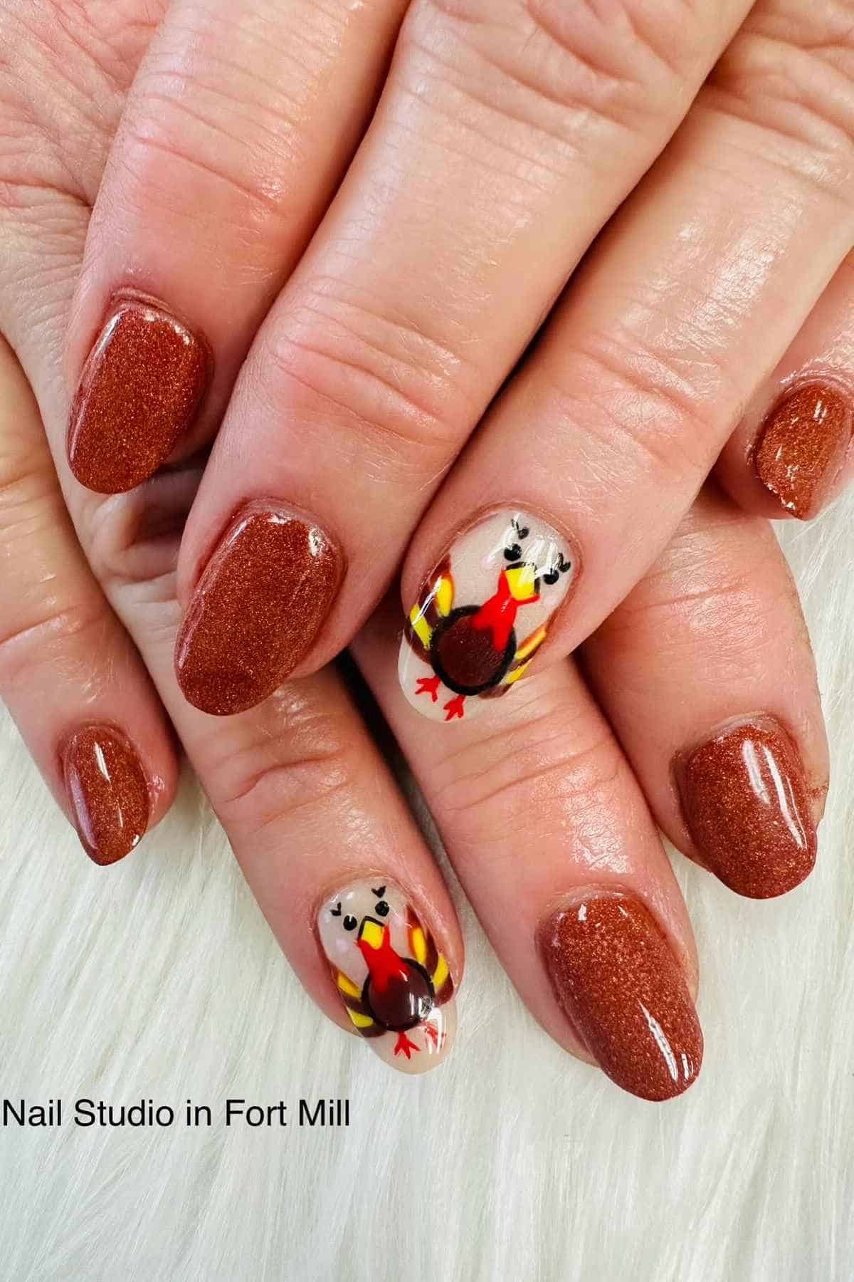 Manicured nails featuring orange glitter polish and accent nails painted with turkey designs.