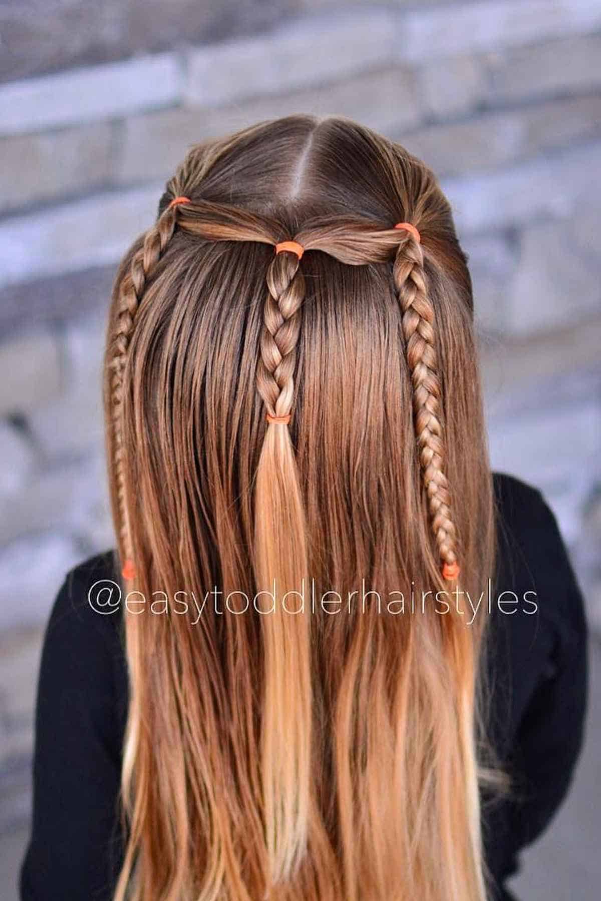 A child’s hair styled with three small braids starting from the crown and secured with orange elastic bands.