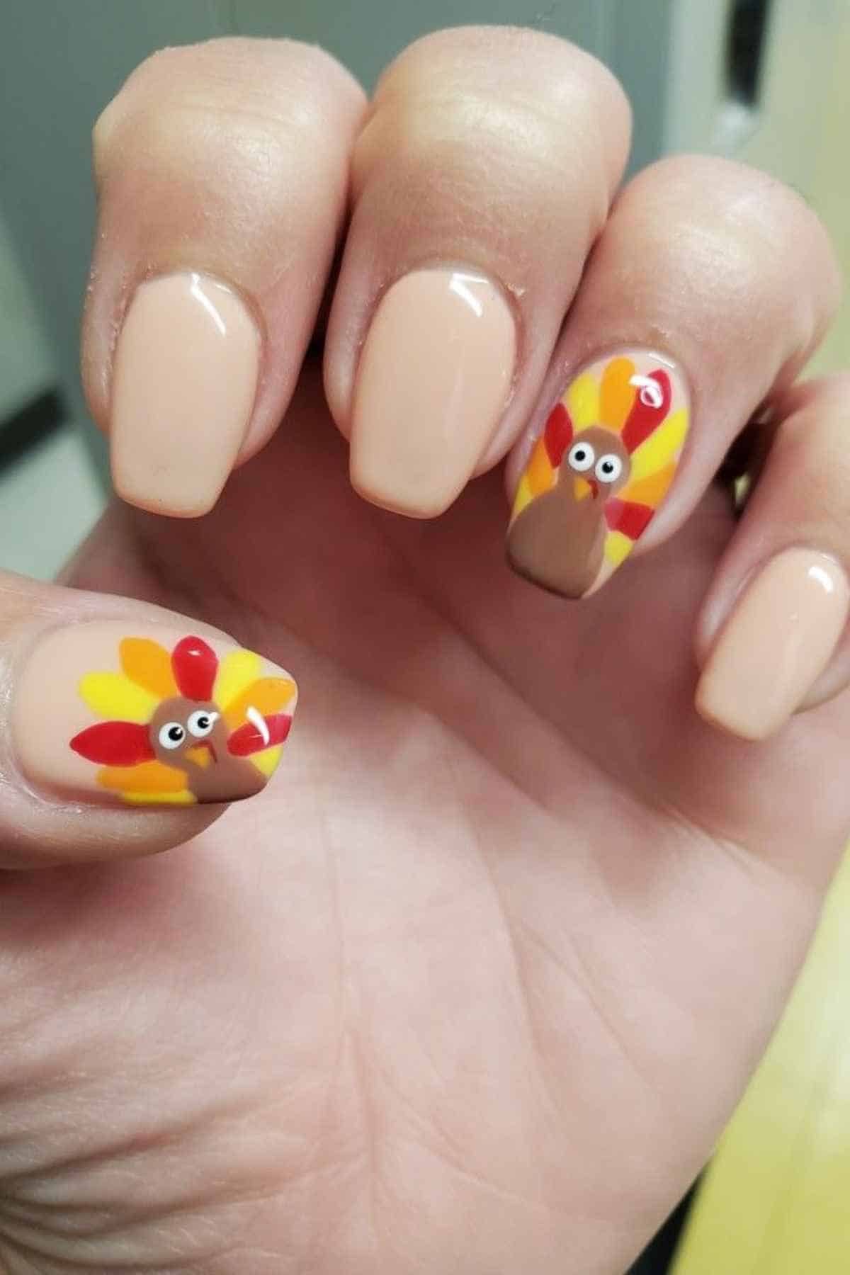Manicured nails painted tan, with two nails featuring painted cartoon turkeys with yellow and red feathers.