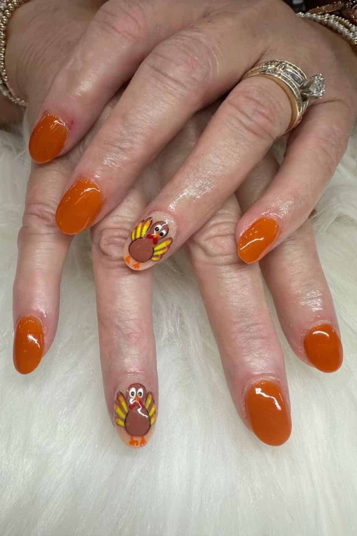 Fingernails painted orange with two nails featuring a turkey design.