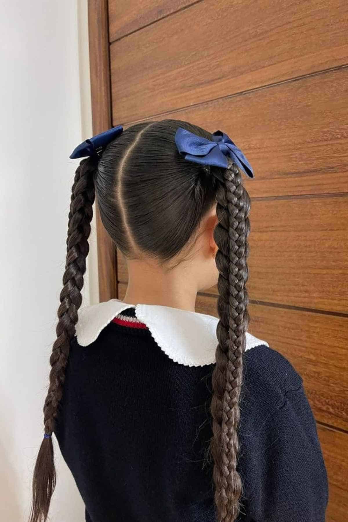 A person with dark hair styled in two long braids with dark blue bows at the top.