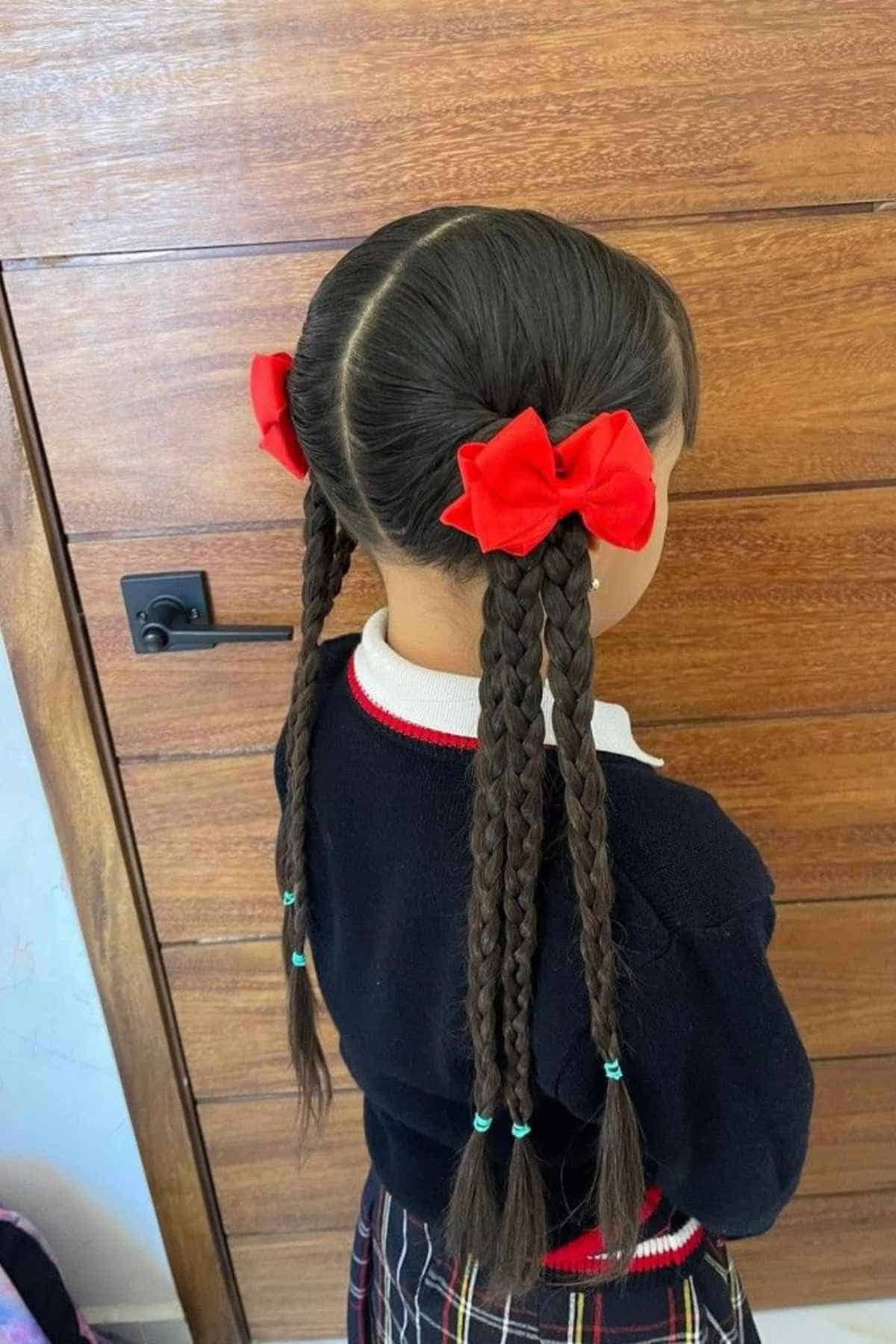 Back view of a child with two braided pigtails, each accented with a large red hair bow.