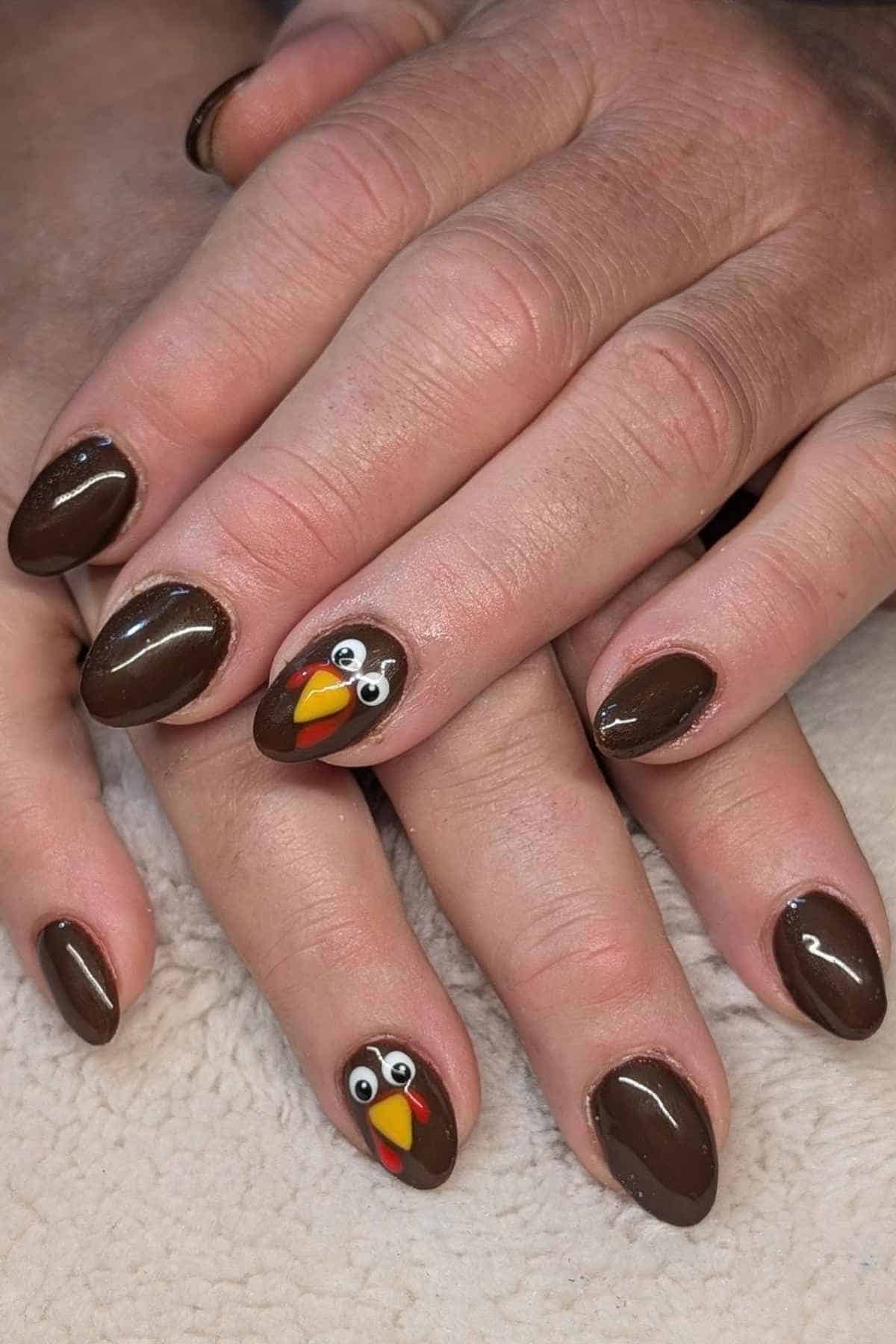 Manicured nails painted brown, with two accent nails featuring a cartoon turkey face design.