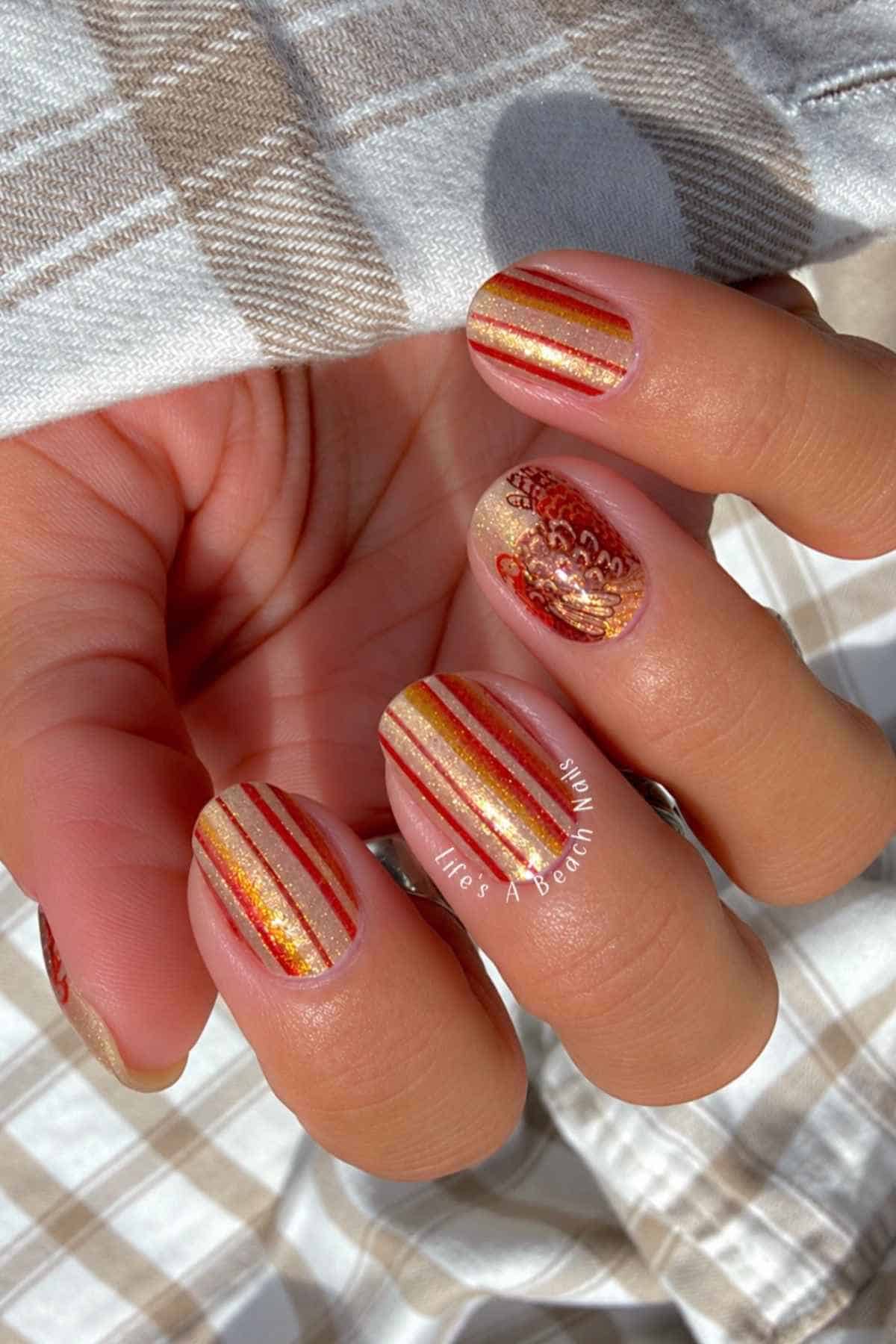 Fingernails painted with alternating red, orange, and gold glitter stripes, featuring an accent nail with a gold floral design.