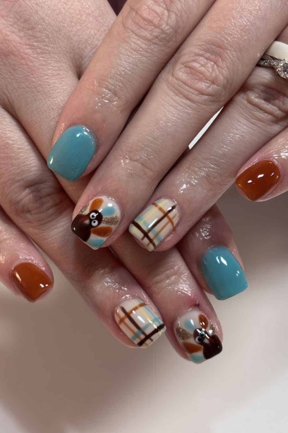Manicured fingernails painted with a mix of solid teal, brown, plaid, and turkey designs.