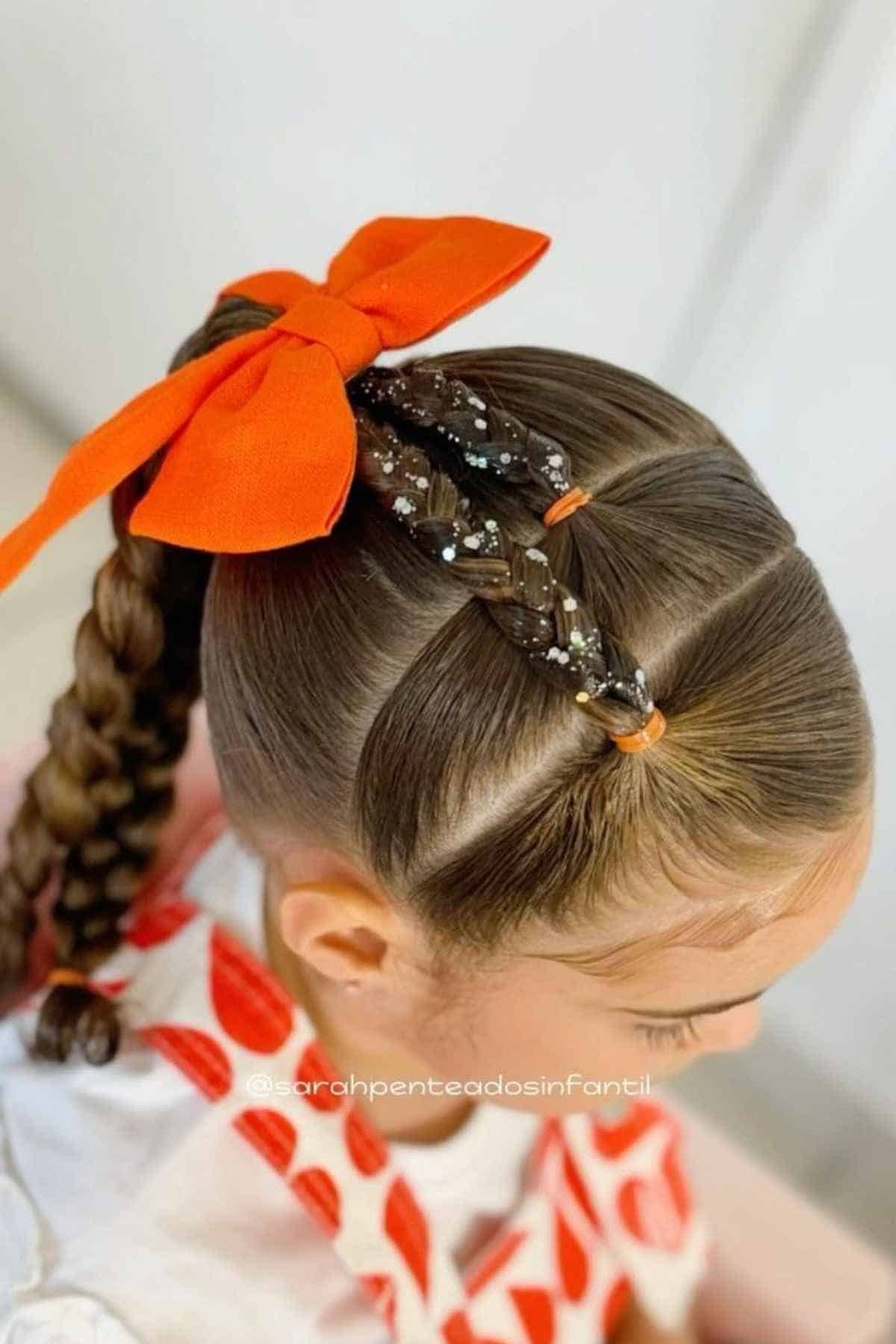 Child’s hair styled in a high ponytail with a large orange bow and two small, glittery braids pulled across the crown of the head.