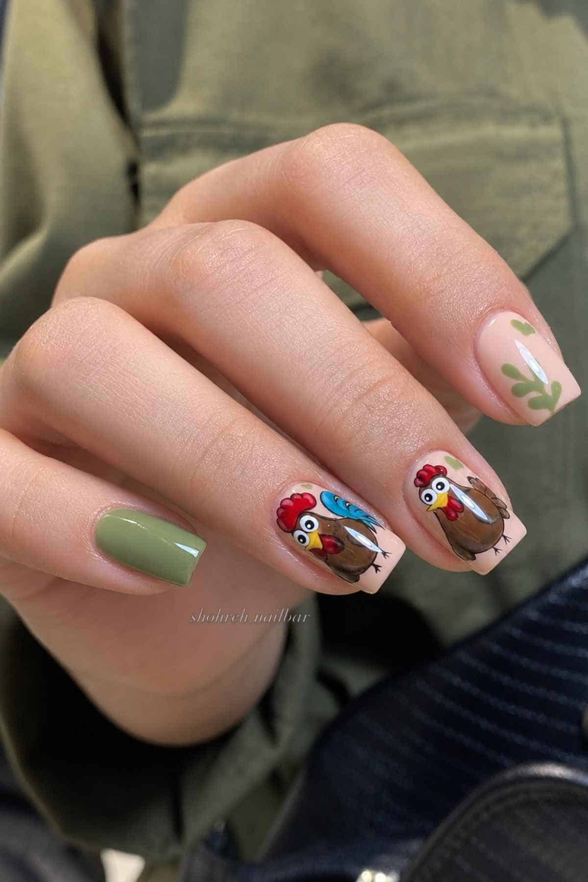 Manicured nails featuring a solid olive green nail, two nails with cartoon turkey designs, and one nail with a green leafy pattern.