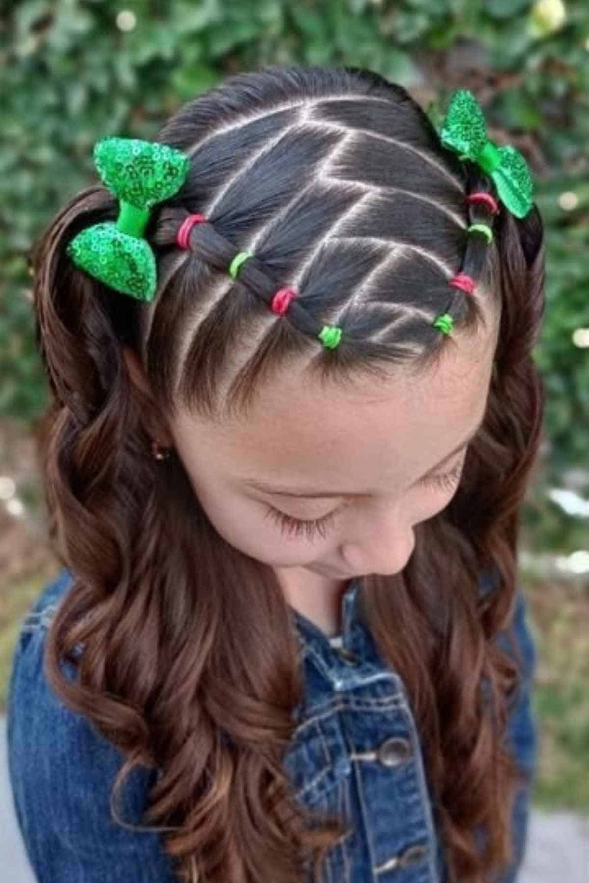 Girl with long brown hair styled in a grid of small sections held by colorful elastics, finished with two green glitter bows and pigtails.