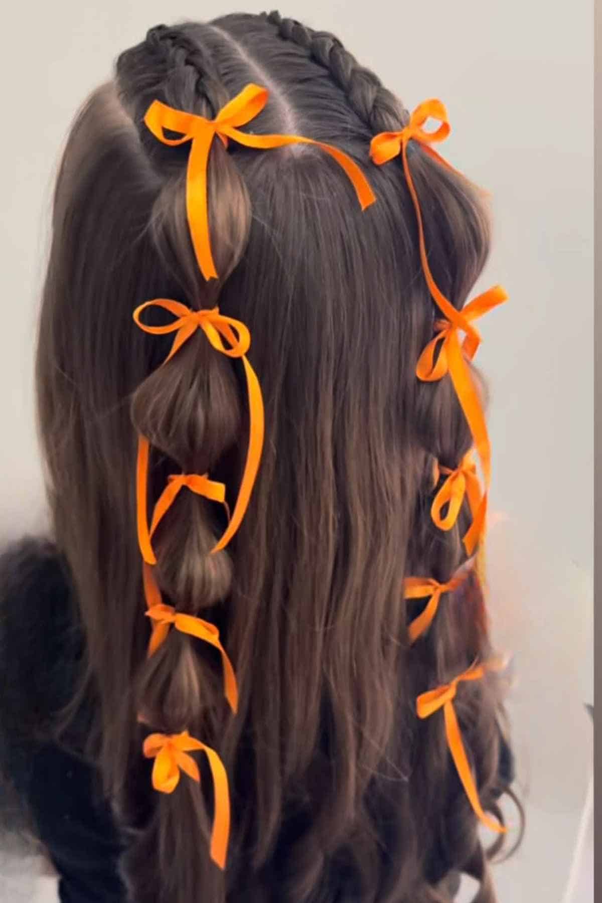 A hairstyle featuring two braided sections decorated with small orange ribbons tied at regular intervals.