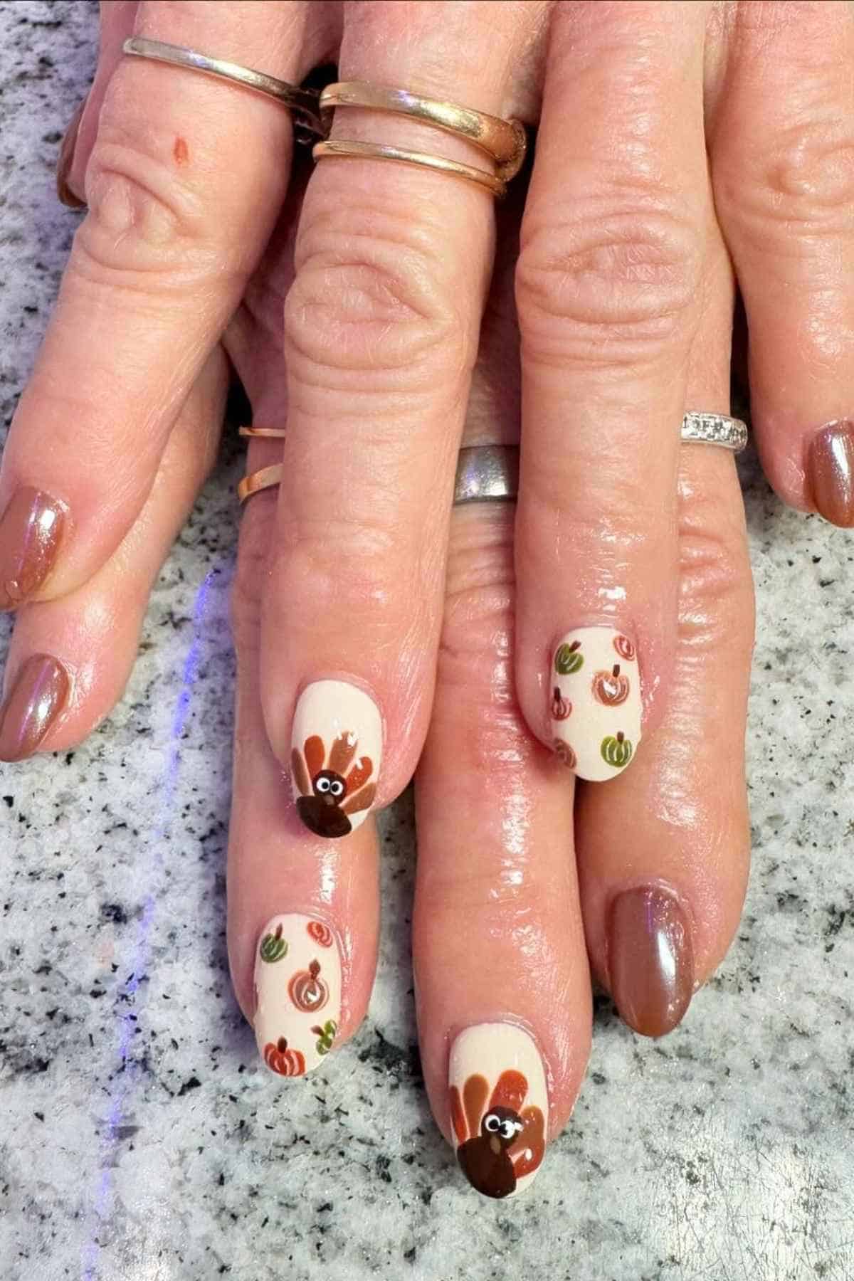 Manicured fingernails painted with brown polish and accent nails featuring turkey and pumpkin designs.
