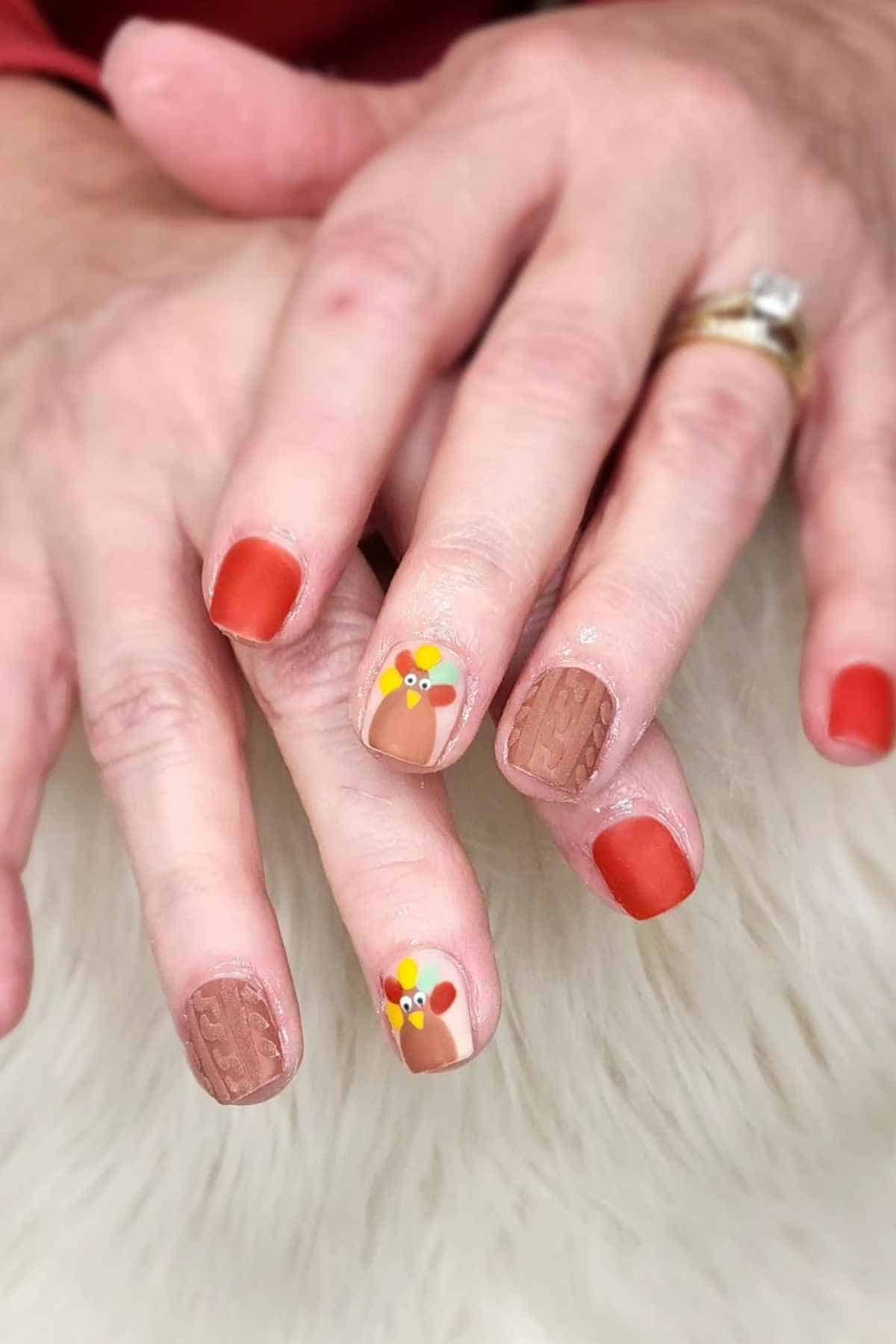 Fingernails painted with a mix of solid matte red, turkey designs, and textured sweater patterns.
