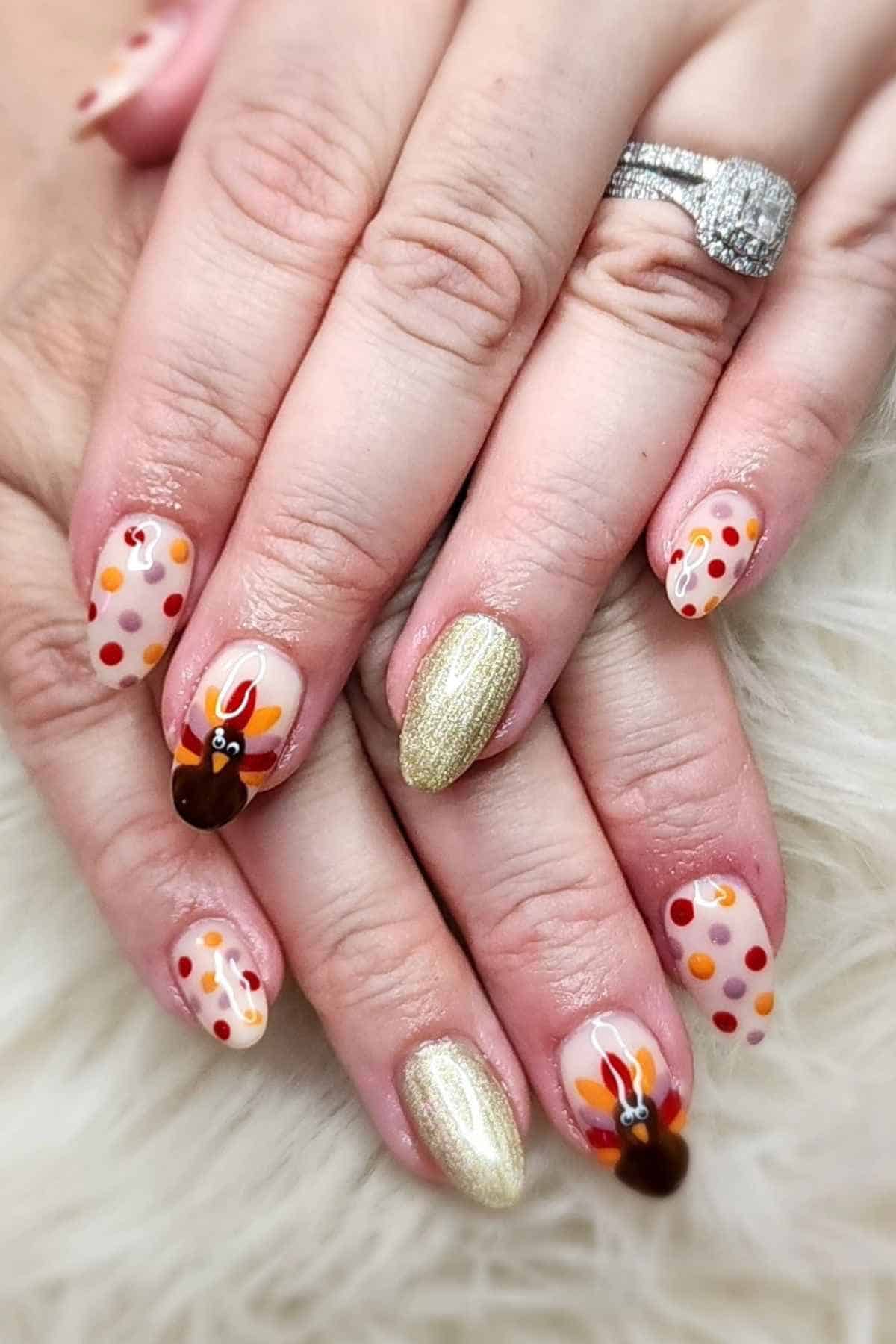 Manicured nails featuring autumn-colored polka dots, two turkey designs, and two solid gold glitter nails.