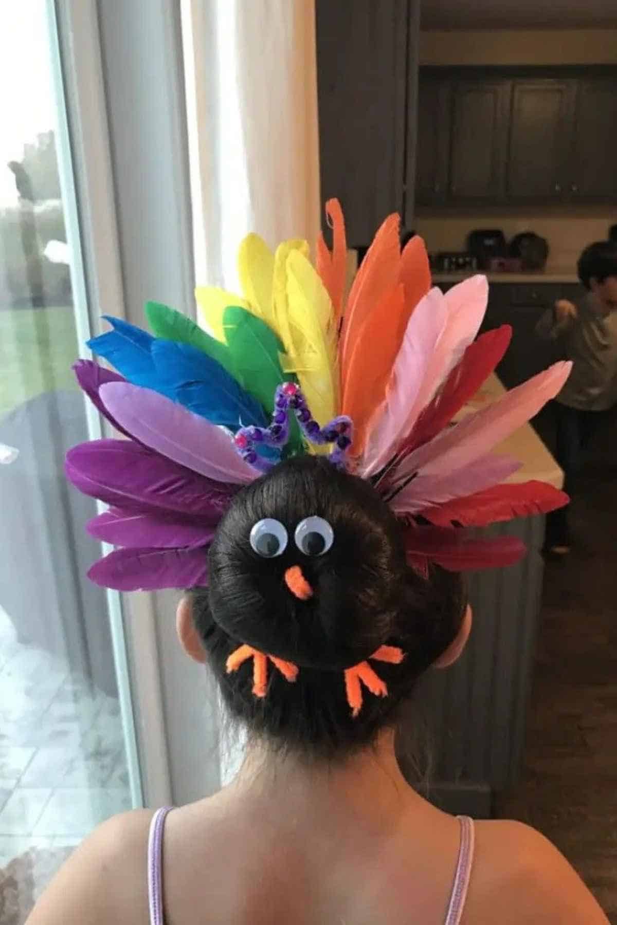 A child’s hair styled into a turkey with googly eyes, a small orange beak, orange feet, and a fan of colorful feathers.