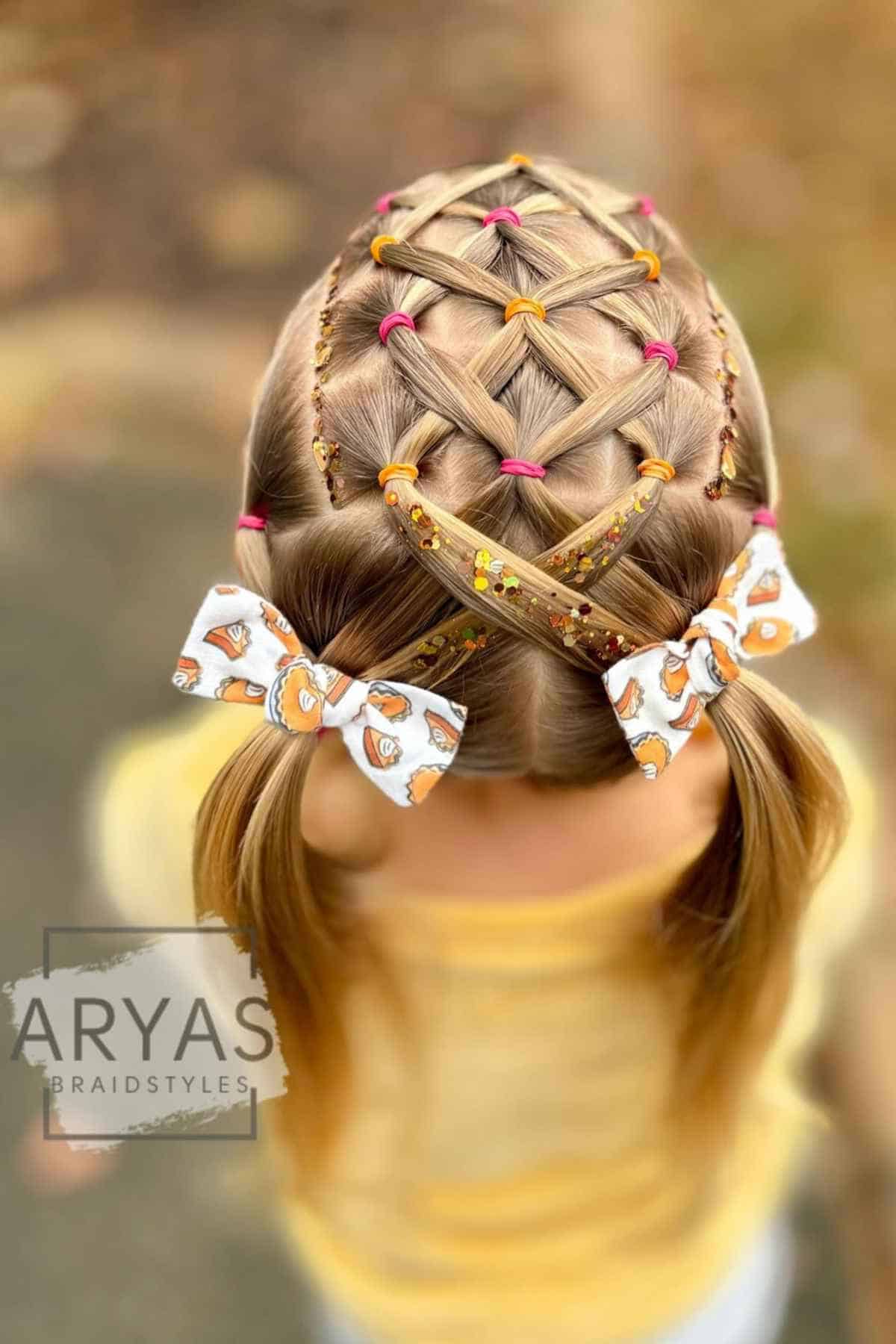 Back view of a child’s hair styled in a lattice braid pattern with colorful hair elastics, glitter, and two bow-patterned hair clips.