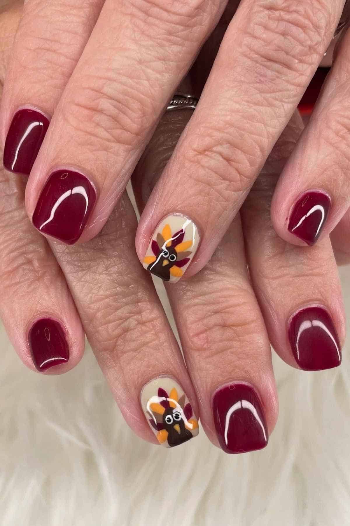 Fingernails painted deep red with two accent nails featuring a cartoon turkey design.
