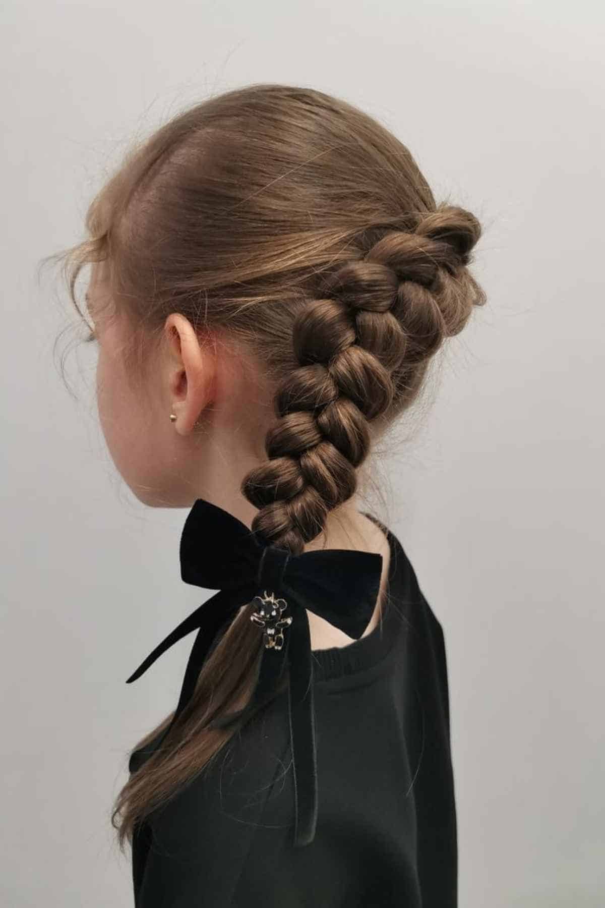 A thick, braided ponytail secured at the base with a black bow featuring a small bear charm.