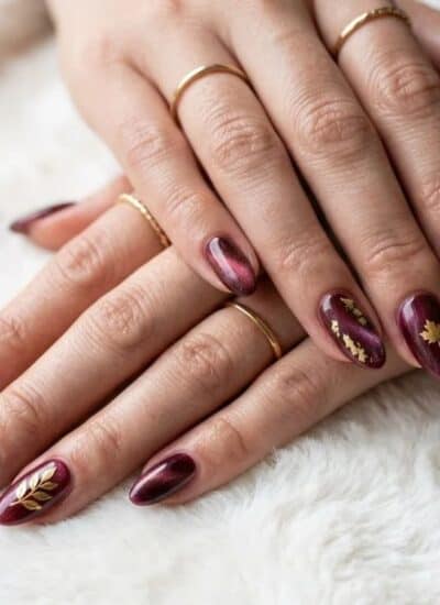 Hands with dark red, cat-eye style manicured nails accented with small gold leaf decals.