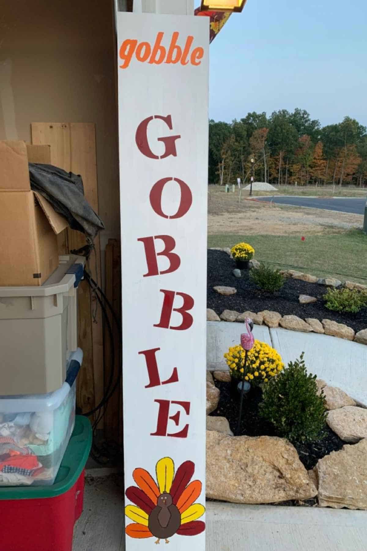 A tall, white vertical sign painted with the word “gobble” in red and orange letters above a cartoon turkey.
