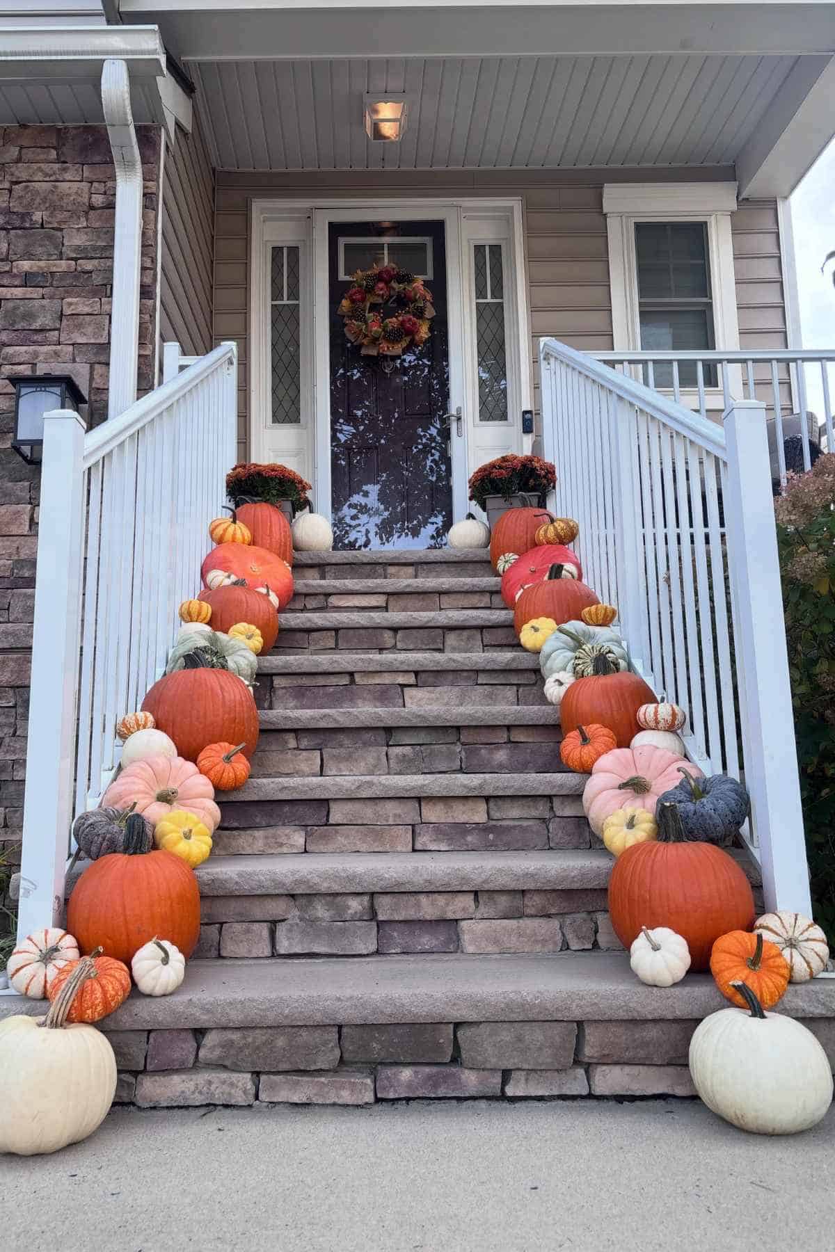 Stone front steps decorated with a variety of orange, white, and blue pumpkins.