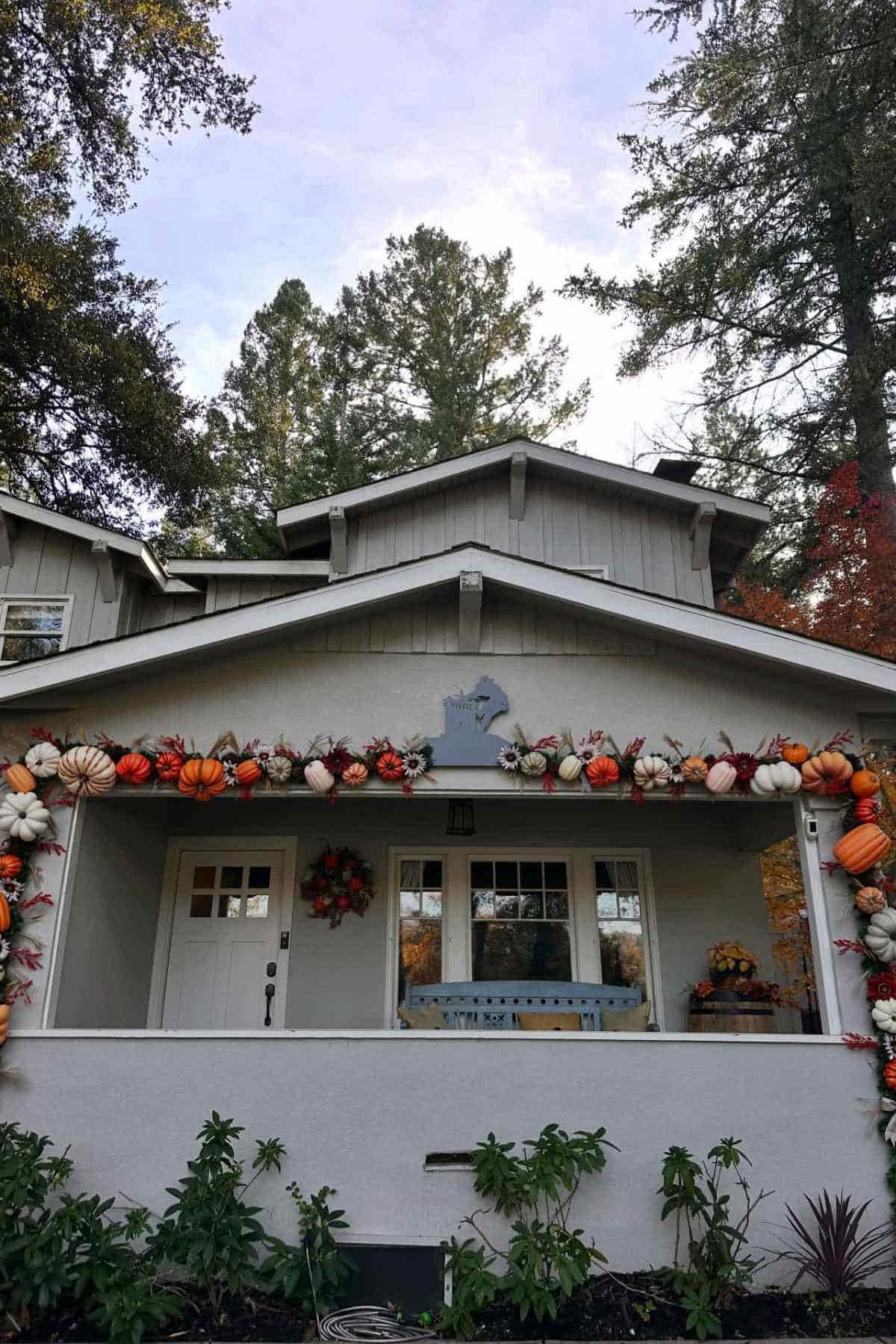 A house exterior decorated for autumn with a garland of pumpkins and fall foliage draped across the front porch roof.