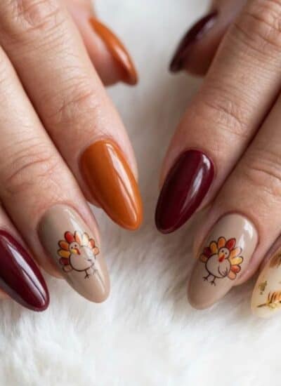 Manicured fingernails painted with fall colors, turkey decals, and feather designs.